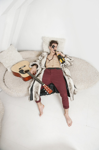 Man with guitar drinking on sofa - Valokuva, kuva