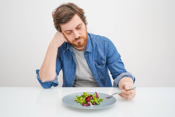 Sad hungry man eating vegetables isolated on white background - Photo, Image