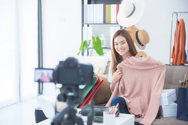 Hermosa mujer asiática blogger mostrando ropa delante de la cámara para grabar vlog video streaming en vivo en su tienda
. - Foto, imagen