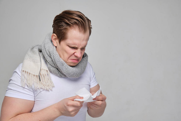 Um homem com uma t-shirt branca estourou o nariz num lenço. O conceito da doença do resfriado comum, gripe
. - Foto, Imagem