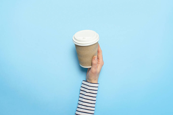 Kadın eli mavi arka planda kahve olan bir kağıt bardak tutuyor. Kahve kavramı, sıcak bir içecek, kahvaltı. Banner Düz yatar, üst görünüm - Fotoğraf, Görsel