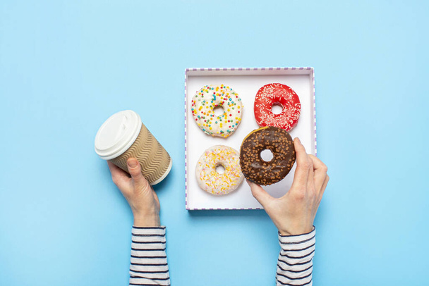 Naiskäsillä on donitsi ja kuppi kahvia sinisellä pohjalla. Konsepti makeiskauppa, leivonnaiset, kahvila. Banneri. Tasainen, ylhäältä
 - Valokuva, kuva