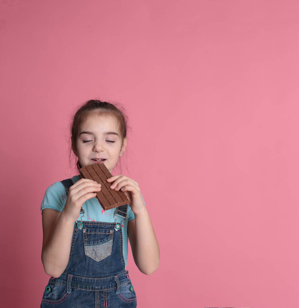 χαμογελαστό χαρούμενο κορίτσι σε μια μεγάλη χαρούμενη διάθεση τρώει γλυκά αντιμετωπίζει σοκολάτα σε ένα φωτεινό ροζ φόντο - Φωτογραφία, εικόνα