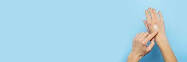 Frauenhände. Frau schmiert Creme auf ihre Hand auf blauem Hintergrund. das Konzept der Kosmetik, Hautpflege, Lotion, Make-up, Wellness. Banner flach gelegt, Ansicht von oben - Foto, Bild