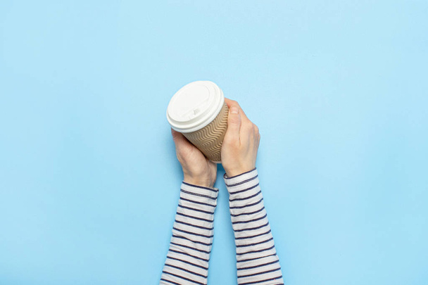 Female hand holds a paper cup with coffee on a blue background. Concept of coffee, a warming drink, breakfast. Banner Flat lay, top view - Foto, afbeelding
