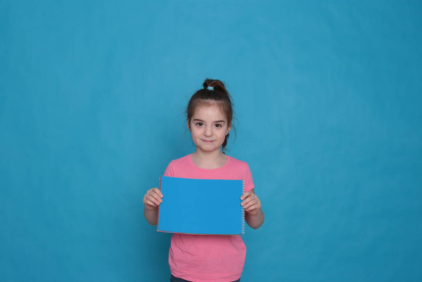 funny girl of eight years old holds a colored sheet of paper free space for writing on a bright background - Photo, Image
