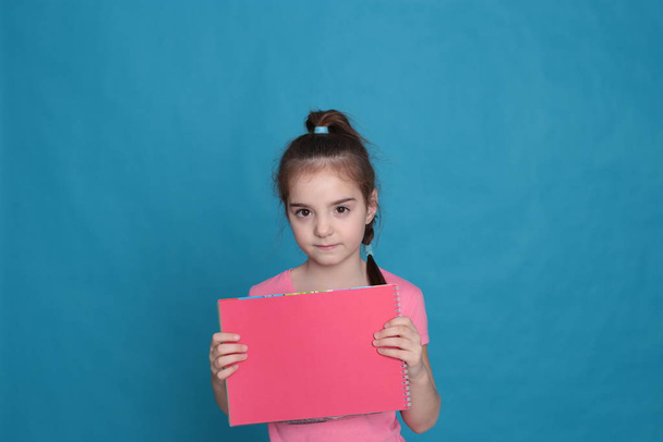 funny girl of eight years old holds a colored sheet of paper free space for writing on a bright background - Foto, Imagen
