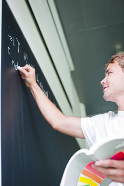 handsome college student solving a math problem during math class in front of the blackboard/chalkboard (color toned image) - Foto, imagen