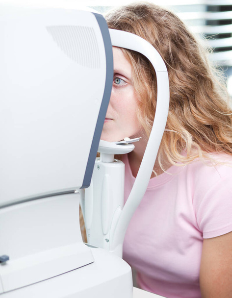 optometry concept - pretty young woman having her eyes examined by an eye doctor (color tuned image - Fotó, kép