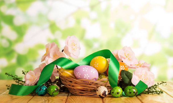 Πασχαλινά αυγά σε καλάθι και εξωτερικό, γρασίδι, λουλούδια, κορδέλα. - Φωτογραφία, εικόνα