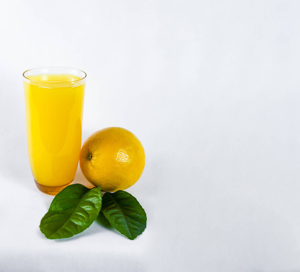 glass of orange juice, orange and orange leaves, on bright background - Фото, зображення