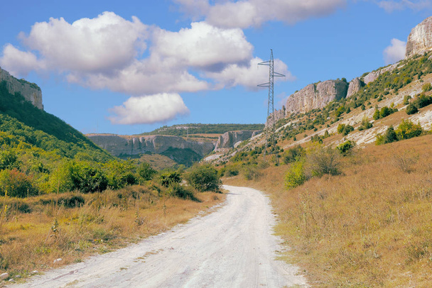 Road in mountains and forested valleys. Blue sky with clouds - Foto, imagen