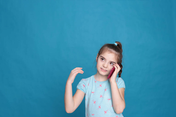 Usmívající se dívka z osmi let drží růžový telefon v rukou na modrém pozadí - Fotografie, Obrázek