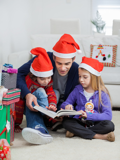 Father And Children In Santa Hats Reading Book - Photo, Image