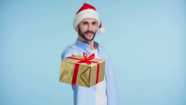 focus pull of man in santa hat with gift απομονωμένο σε μπλε - Πλάνα, βίντεο