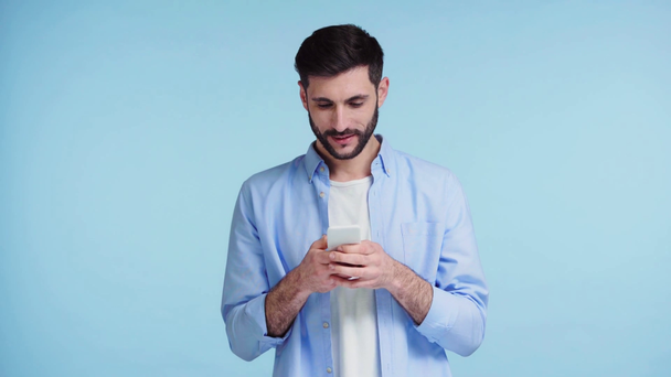 γενειοφόρος άντρας που χρησιμοποιεί smartphone απομονωμένο σε μπλε  - Πλάνα, βίντεο
