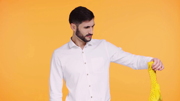 niezadowolony mężczyzna trzymając śmierdzące skarpetki odizolowane na pomarańczowo  - Materiał filmowy, wideo