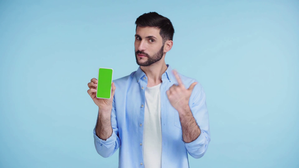 man wijzend met vinger naar smartphone met groen scherm geïsoleerd op blauw - Video