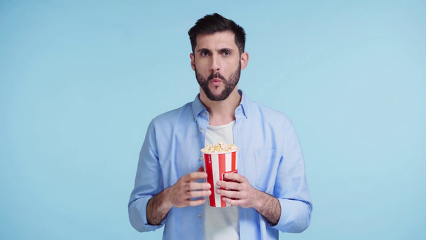 ember eszik popcorn és néz film elszigetelt a kék - Felvétel, videó