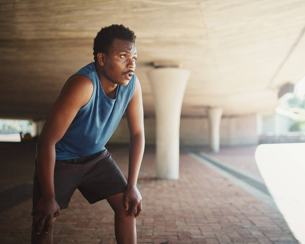 An african american male runner grasping breathe after running on street under the bridge in morning - 写真・画像