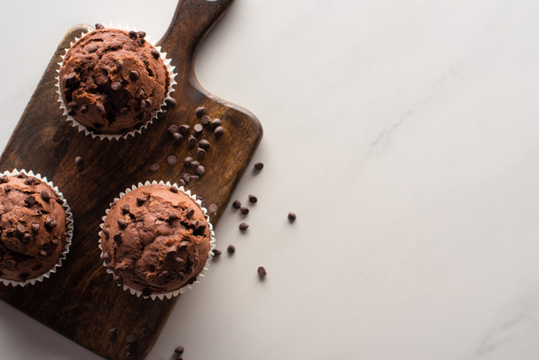 top view of fresh chocolate muffins on wooden cutting board on marble surface - Foto, immagini