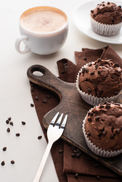 fresh chocolate muffins on wooden cutting board near napkin, fork and coffee - Foto, Imagen
