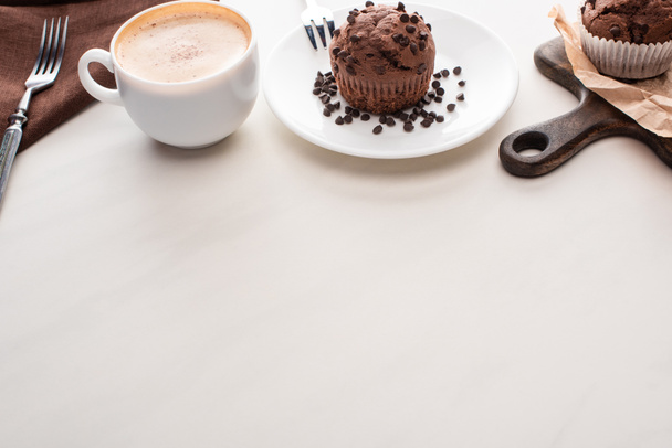 fresh chocolate muffins on wooden cutting board and plate with forks near coffee - Photo, Image