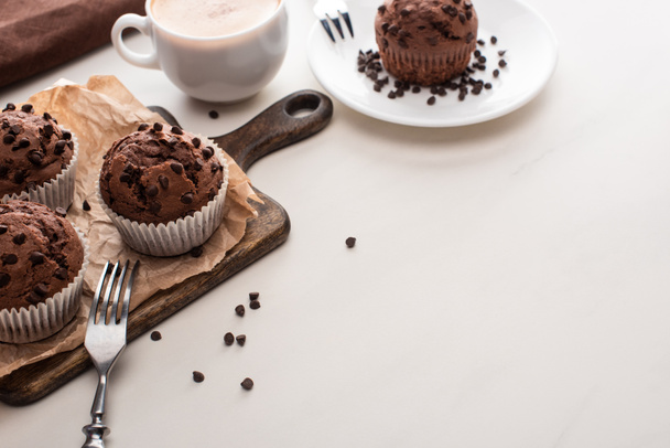 fresh chocolate muffins on wooden cutting board and plate with forks near coffee - Foto, Bild