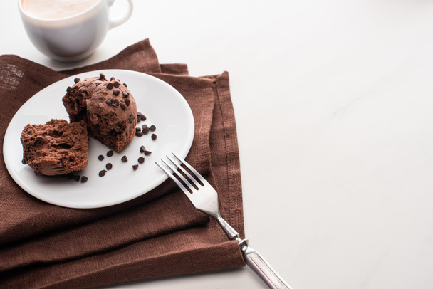 fresh chocolate muffins on plate with fork on brown napkin near coffee - Фото, изображение