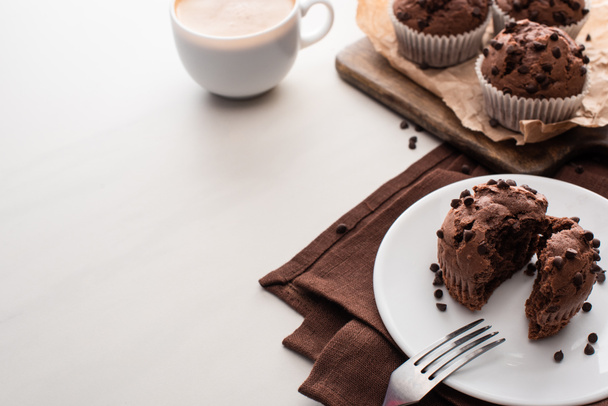 fresh chocolate muffins on wooden cutting board near plate with fork and coffee - Foto, afbeelding