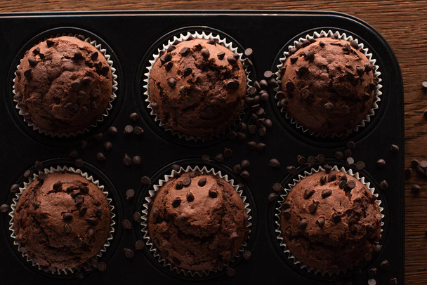 top view of fresh chocolate muffins in muffin tin on wooden surface - Foto, Bild