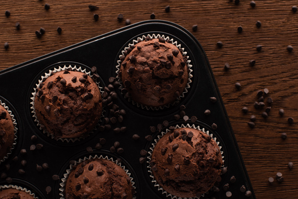 vrchní pohled na čerstvé čokoládové muffiny v muffinovém cínu na dřevěném povrchu - Fotografie, Obrázek