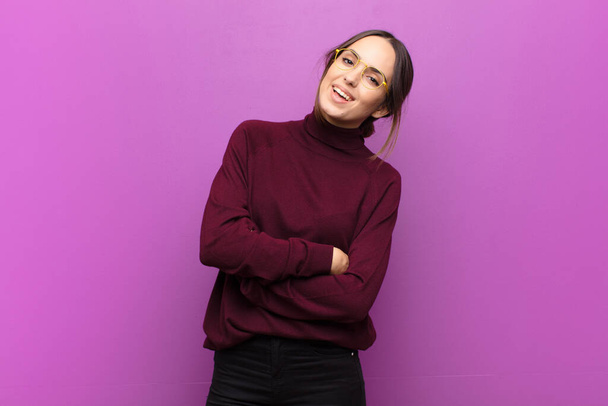 young pretty woman laughing happily with arms crossed, with a relaxed, positive and satisfied pose against purple wall - Foto, afbeelding