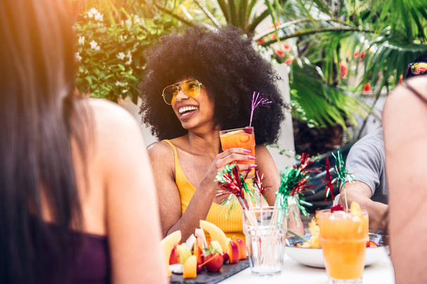 Χαρούμενη μαύρη όμορφη γυναίκα που διασκεδάζει πίνοντας κοκτέιλ με φίλους σε εξωτερικούς χώρους. Ομάδα χιλιετιών γελάνε μαζί σε ένα πάρτι. - Φωτογραφία, εικόνα
