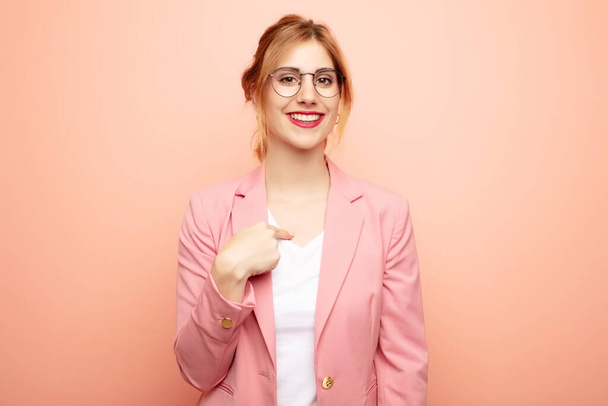 young pretty blonde woman looking happy, proud and surprised, cheerfully pointing to self, feeling confident and lofty. business concept - 写真・画像