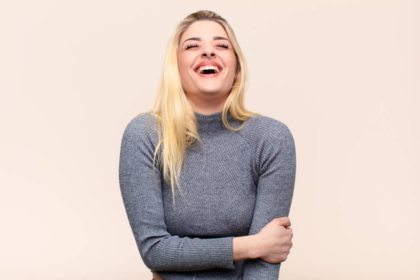 young pretty blonde woman laughing shyly and cheerfully, with a friendly and positive but insecure attitude against flat wall - Фото, зображення