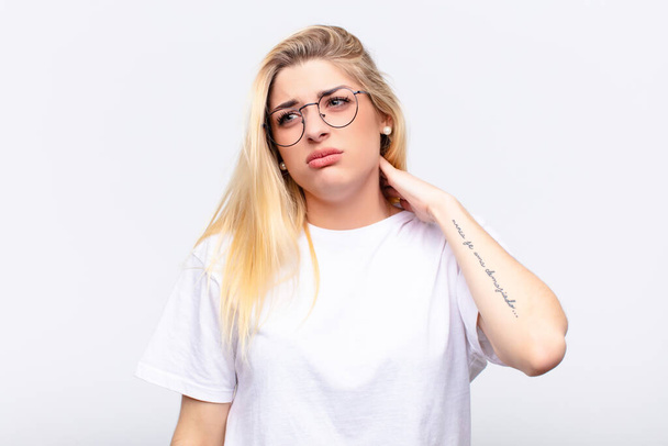 young pretty blonde woman feeling stressed, frustrated and tired, rubbing painful neck, with a worried, troubled look against white wall - Foto, Imagen