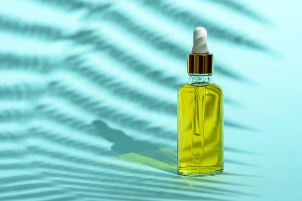 bottiglia di vetro con pipetta con olio cosmetico giallo su fondo blu con ombra
 - Foto, immagini