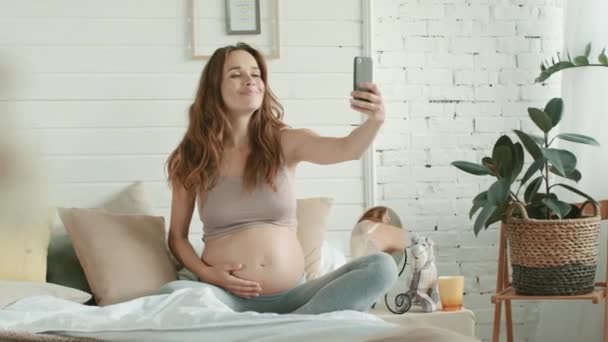 Lähikuva odottaa äiti ottaa puhelimen selfie hänen vatsa sängyssä
. - Materiaali, video