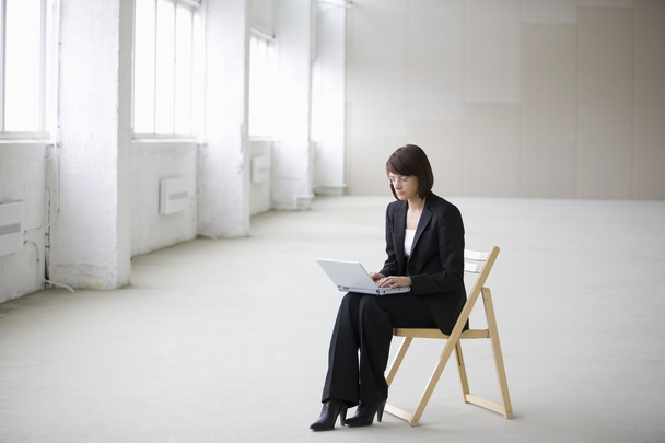 Business woman works on laptop in empty warehouse - Фото, изображение