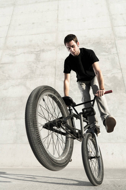Young BMX bicycle rider on a grey urban concrete background - Fotoğraf, Görsel