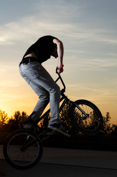 Young BMX bicycle rider on a sunset sky background - Fotó, kép
