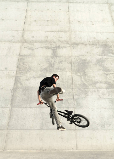 Young BMX bicycle rider on a grey urban concrete background - Valokuva, kuva