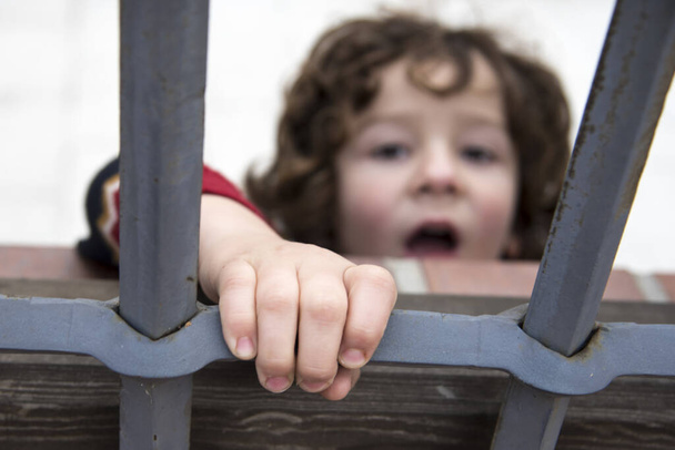 garotinho sorridente trancado atrás de uma cerca de ferro
 - Foto, Imagem