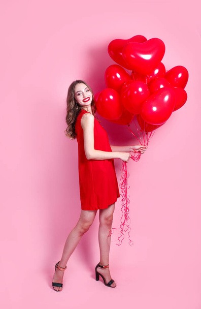 Beautiful emotional girl in red dress with red heart ballons on pink background - Fotografie, Obrázek
