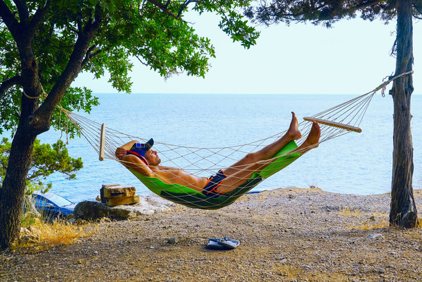 Молодий чоловік відпочиває в гамаку на пляжі
 . - Фото, зображення