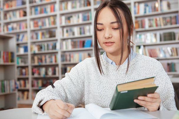 Houkutteleva aasialainen nainen opiskelee kirjastossa
 - Valokuva, kuva