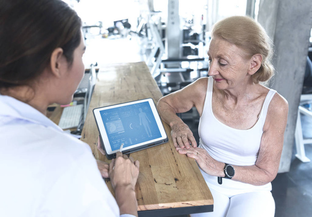 Médecin avec la femme âgée dans le centre de réadaptation vérifier les soins de santé et de montrer des données quelque chose sur Tablet
. - Photo, image