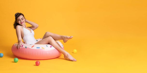 Happy young woman dressed in swimwear posing with rubber ring in yellow banner background with copy space. - Valokuva, kuva
