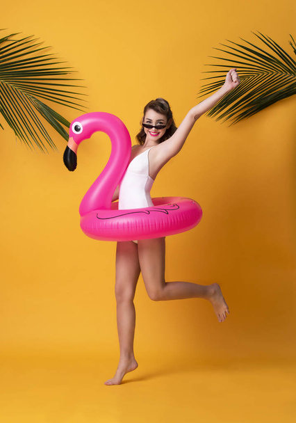 Feliz mulher sorridente vestida de roupa de banho segurando anel de borracha flamingo e desfrutando de sua fuga de férias de verão em fundo amarelo
. - Foto, Imagem